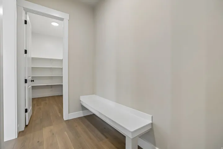 Entryway featuring a built-in white bench, wood-finish flooring, and a pantry with multiple shelves