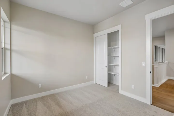 Carpeted room featuring a white bi-fold closet with built-in shelving, white trim, and light beige walls