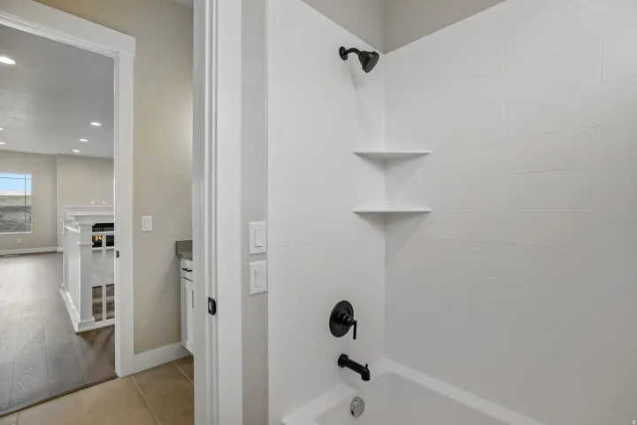 Bathtub with matte black fixtures, white subway tile surround, and integrated corner shelving