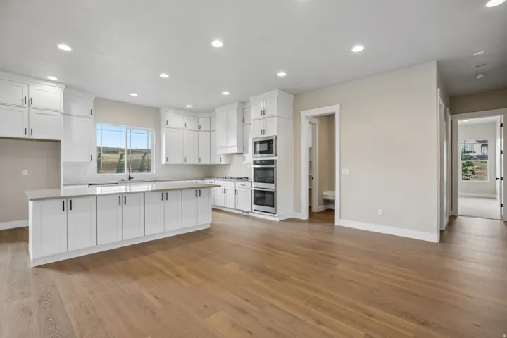 Modern open-concept kitchen featuring extensive white cabinetry, a large central island with countertop seating, stainless steel double wall ovens, and wood-finish flooring throughout