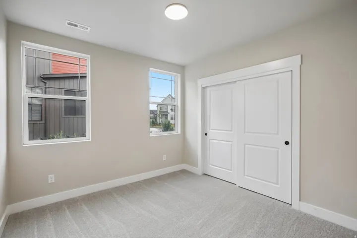 Carpeted room featuring two large windows, a sliding door closet with matte black hardware, white trim, and light neutral wall paint
