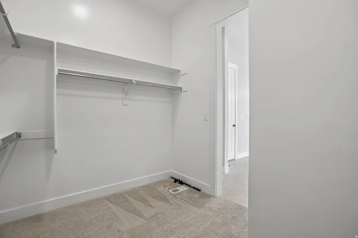 Spacious closet featuring built-in shelving, hanging rods, light-colored carpet, white baseboards, and a doorway opening to an interior space