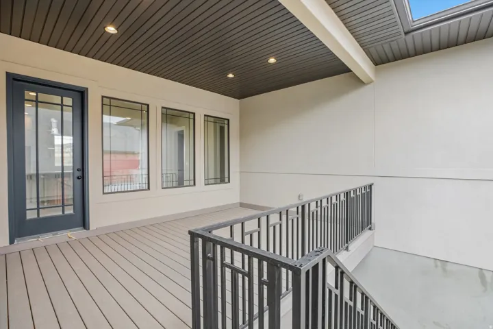 Covered outdoor deck with composite wood-finish flooring, featuring a dark-framed glass paneled door and three transom windows