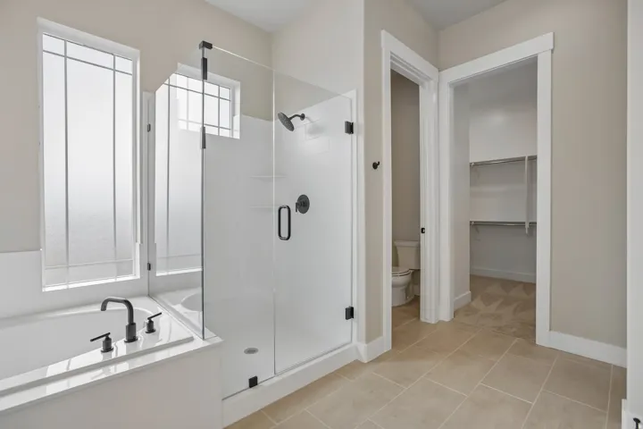 Bathroom featuring a glass-enclosed shower, a built-in tub with matte black fixtures, and privacy windows