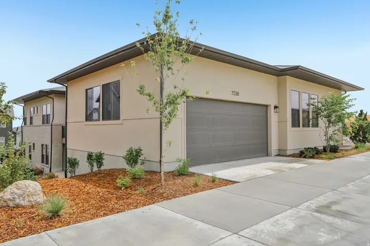 Contemporary exterior featuring a two-car garage with a gray door, stucco siding, and dark trim details