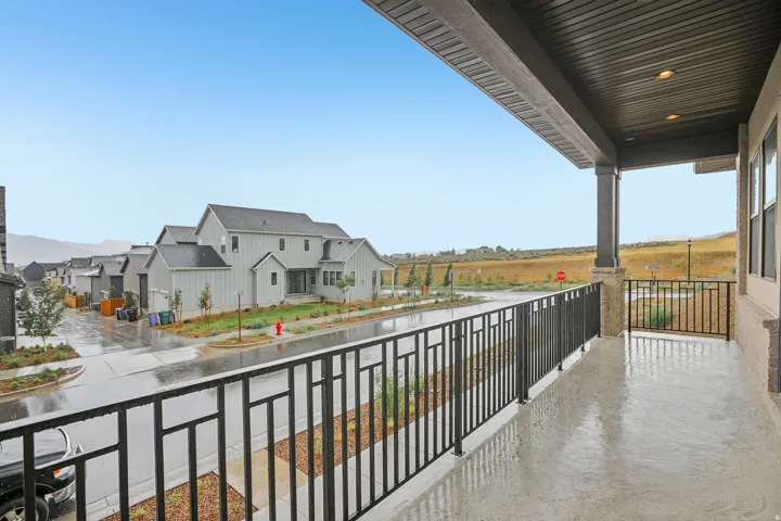 Spacious covered balcony featuring a textured concrete surface, black metal railings, and recessed lighting