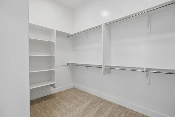 Walk-in closet featuring built-in shelving, dual hanging rods, and neutral-toned carpet flooring