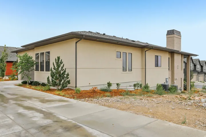 Contemporary stucco exterior featuring a large concrete driveway, dark-framed windows, a prominent brick chimney, and a dark shingle roof