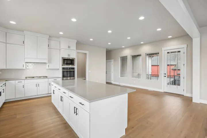 Open-concept kitchen and living area featuring a large center island with a light-toned countertop, white cabinetry with matte black hardware, stainless steel appliances, and light wood-finish flooring
