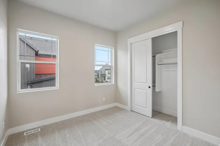 Neutral-toned room featuring a light gray carpet, two windows with white trim, and a sliding closet with white doors