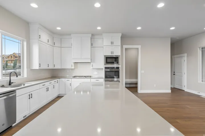 Spacious kitchen featuring an extended island with a light-toned countertop, white cabinetry with dark hardware, stainless steel appliances, recessed lighting, and wood-finish flooring