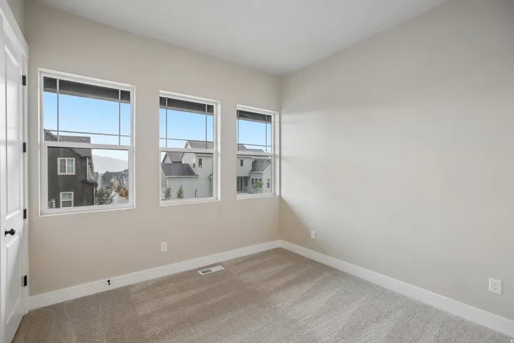 Bright interior space featuring three large windows, neutral-toned carpeting, light-colored walls, white trim, and a white door with black hardware