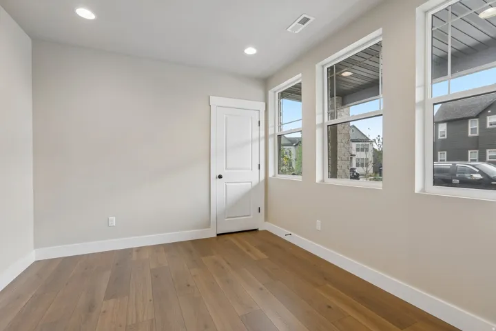 Light-filled room featuring wood-finish flooring, recessed lighting, white baseboards, and multiple large windows with white trim