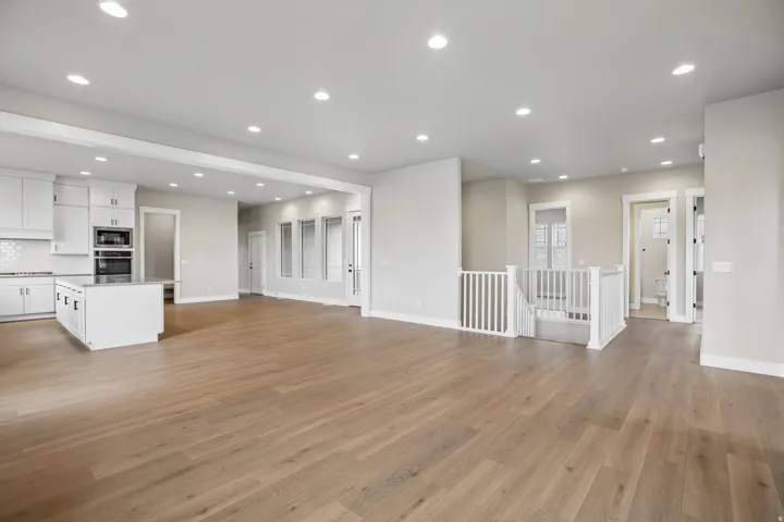 Open-concept living area featuring light wood-finish flooring, recessed ceiling lighting, and a kitchen with white cabinetry, a central island, and stainless steel built-in appliances