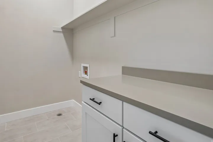 Laundry area featuring a durable countertop, white cabinetry with matte black hardware, and a tile floor