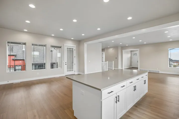 Open-concept living area featuring a large kitchen island with a light-toned countertop, white cabinetry with dark hardware, wood-finish flooring, and recessed lighting