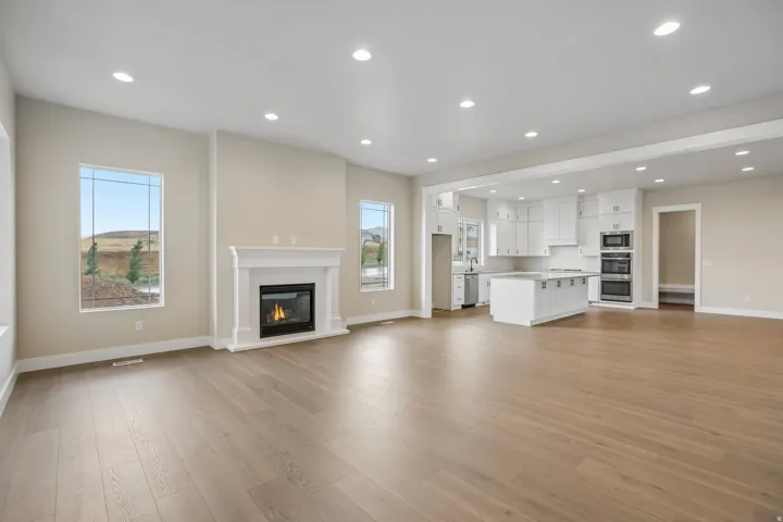 Expansive open-concept living area featuring wood-finish flooring, recessed lighting, and a white mantel fireplace