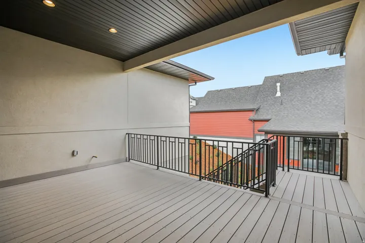 Spacious outdoor deck featuring light-toned composite decking, a dark metal railing with geometric patterns, and a dark slatted ceiling with recessed lighting