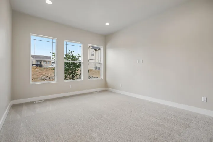 Spacious room featuring three large windows, light gray carpeting, neutral wall finishes, bright white baseboards, and recessed lighting