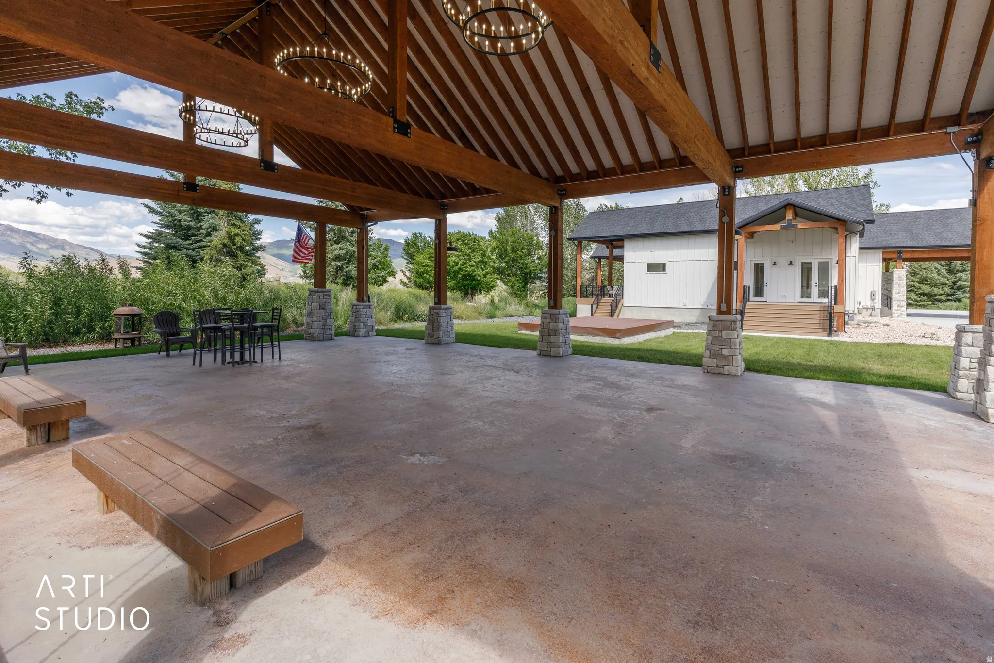 Expansive covered outdoor structure featuring exposed wood beams, a vaulted ceiling, and decorative iron chandeliers