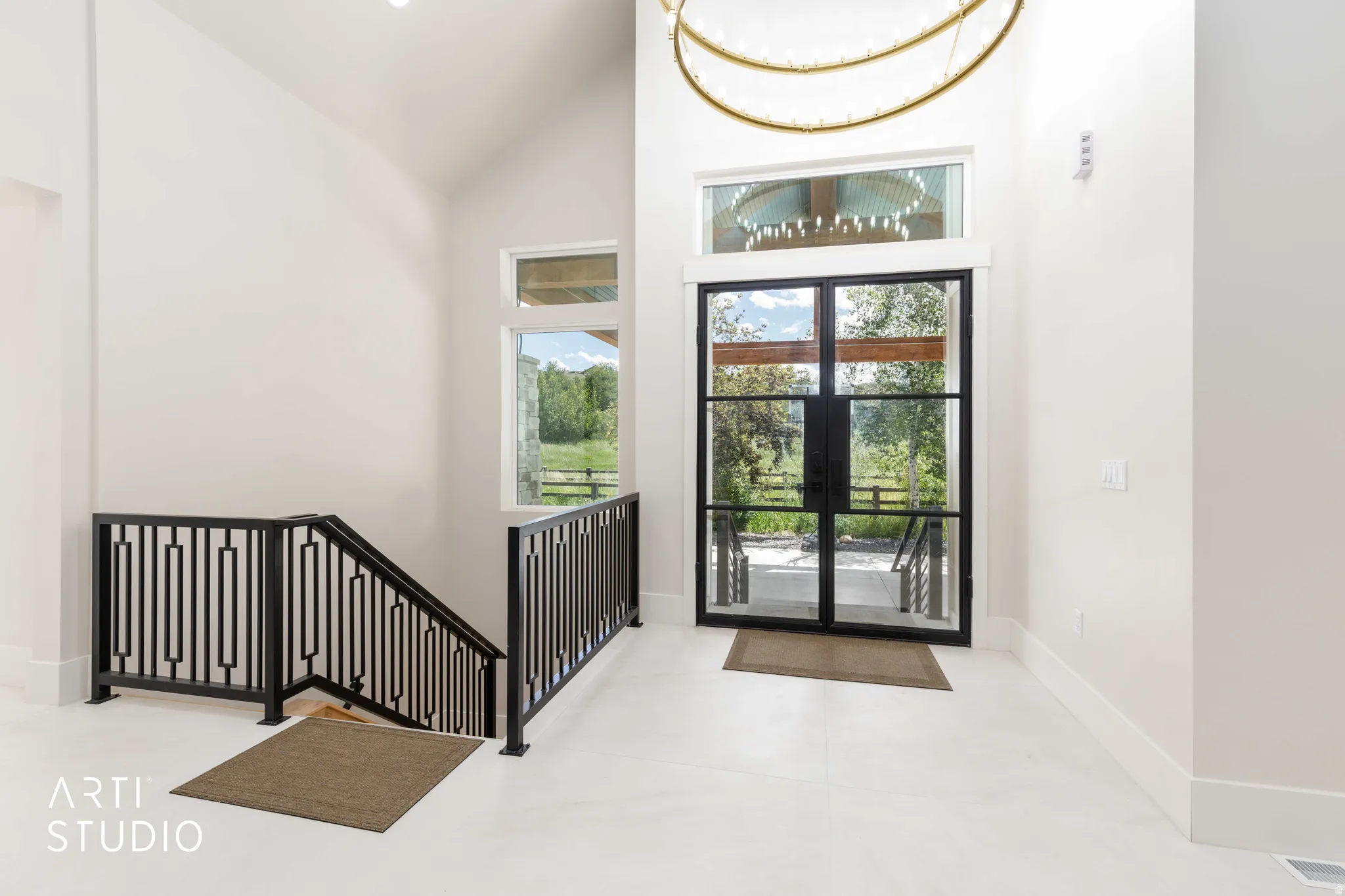 Entryway featuring a double iron and glass front door with transom window, vaulted ceiling, contemporary chandelier, and a black iron-railed staircase