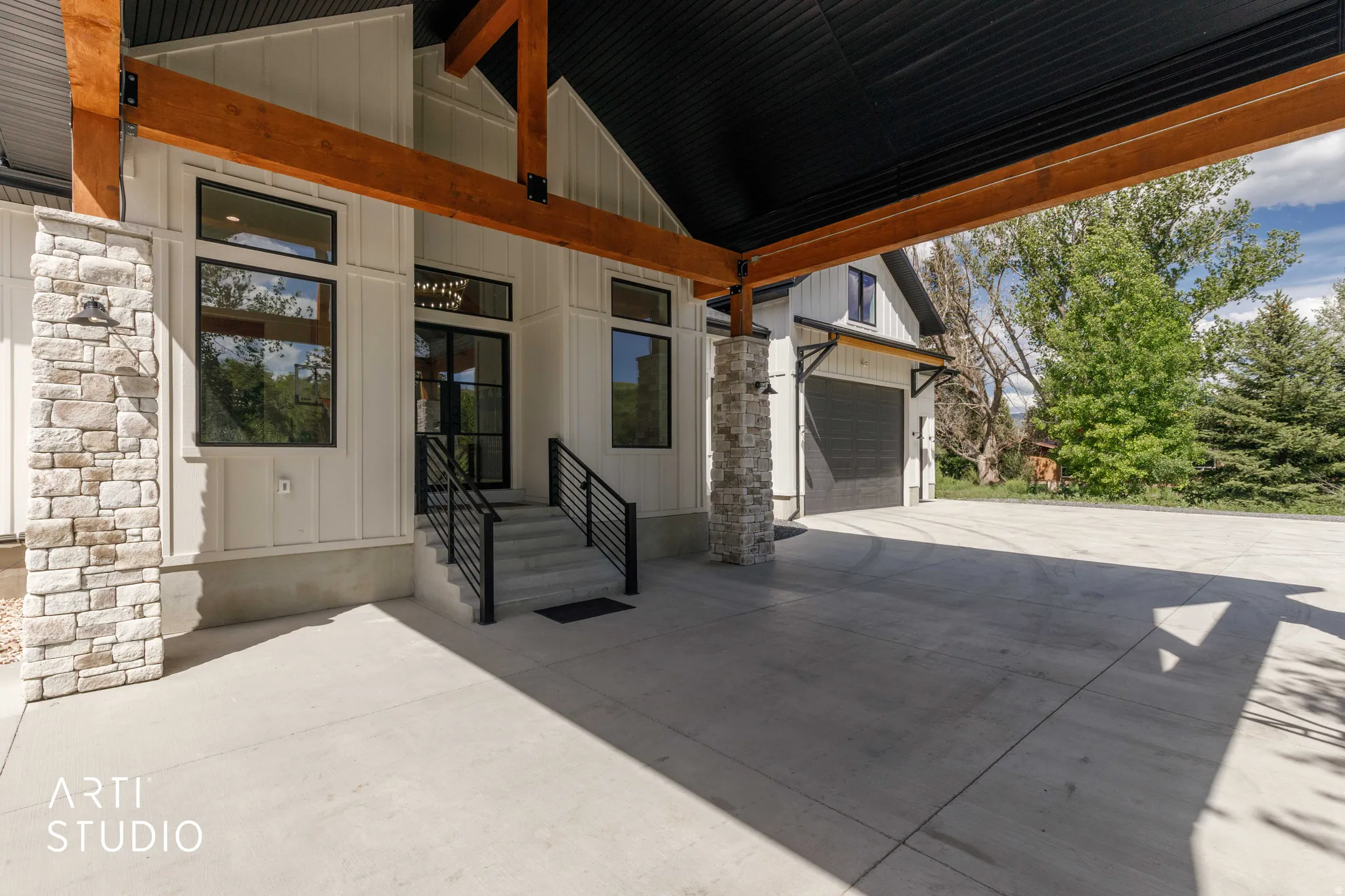 Covered entryway featuring board-and-batten siding, stone veneer accents, wood beams, and a concrete drive