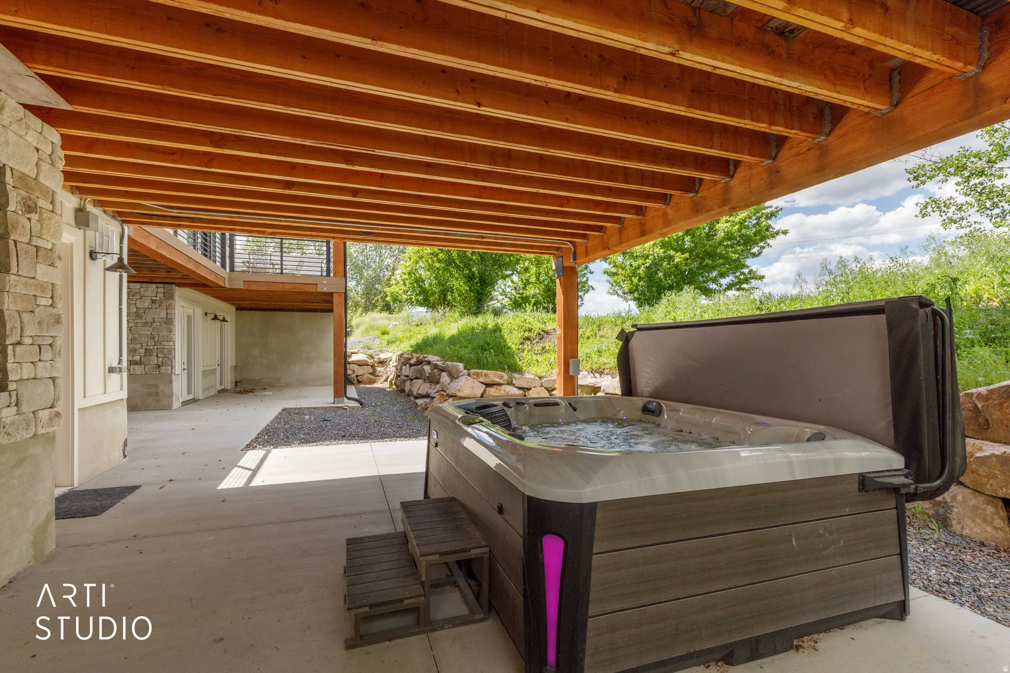 Covered patio area featuring a built-in spa with steps, exposed wood beam ceiling, stone accent wall, and concrete flooring