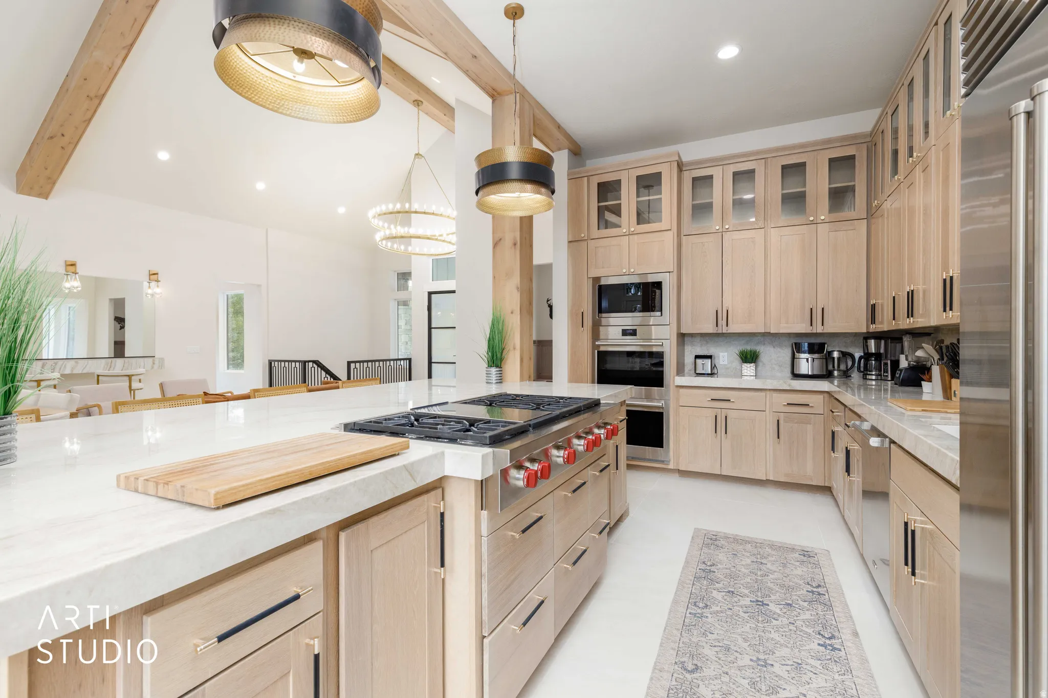 Gourmet kitchen featuring a large central island with a built-in gas range, light wood cabinetry, stone countertops, stainless steel appliances, and a tiled backsplash