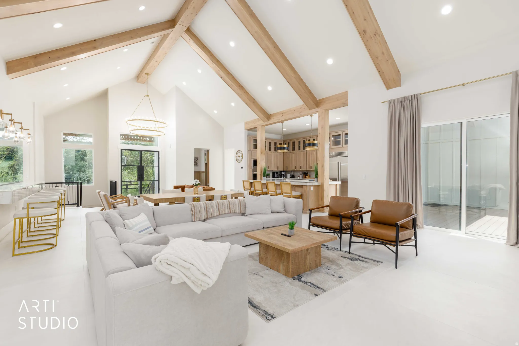 Spacious open-concept living area featuring vaulted ceilings with exposed wood beams, recessed lighting, and expansive glass sliding doors