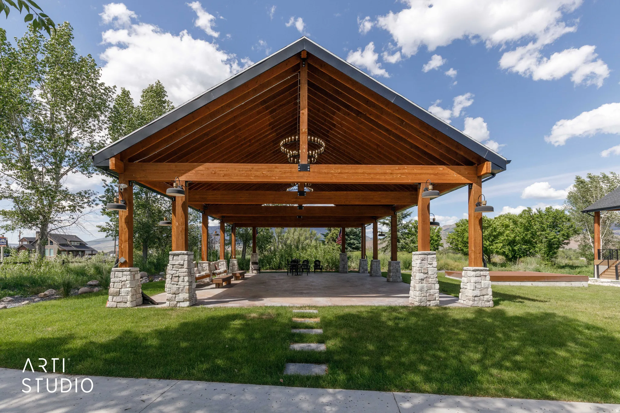 Expansive outdoor pavilion featuring a vaulted wood-finish ceiling, exposed timber beams, stone-clad columns, and a paved concrete floor