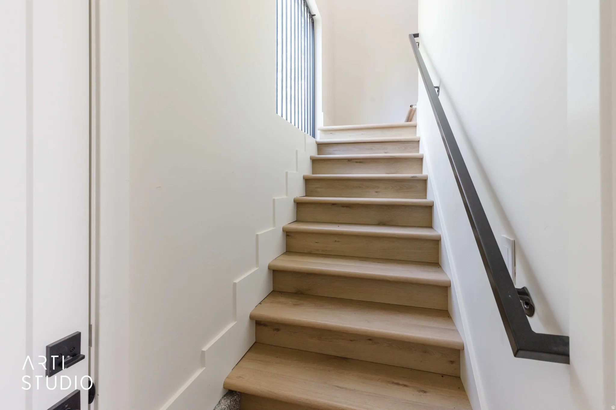 Staircase featuring wood-finish treads, white risers, a matte black handrail, and vertical balusters