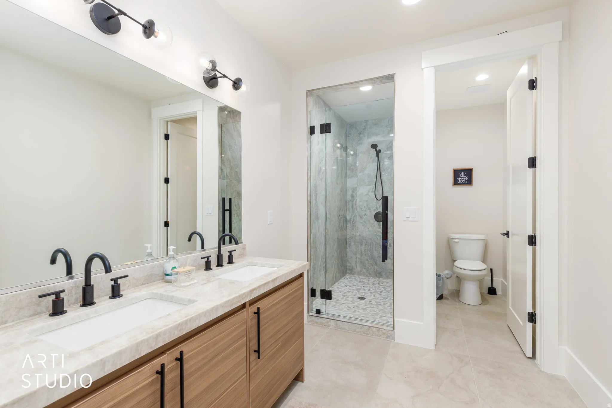 Bathroom featuring a dual vanity with light-toned countertop, wood-finish cabinetry, and matte black fixtures