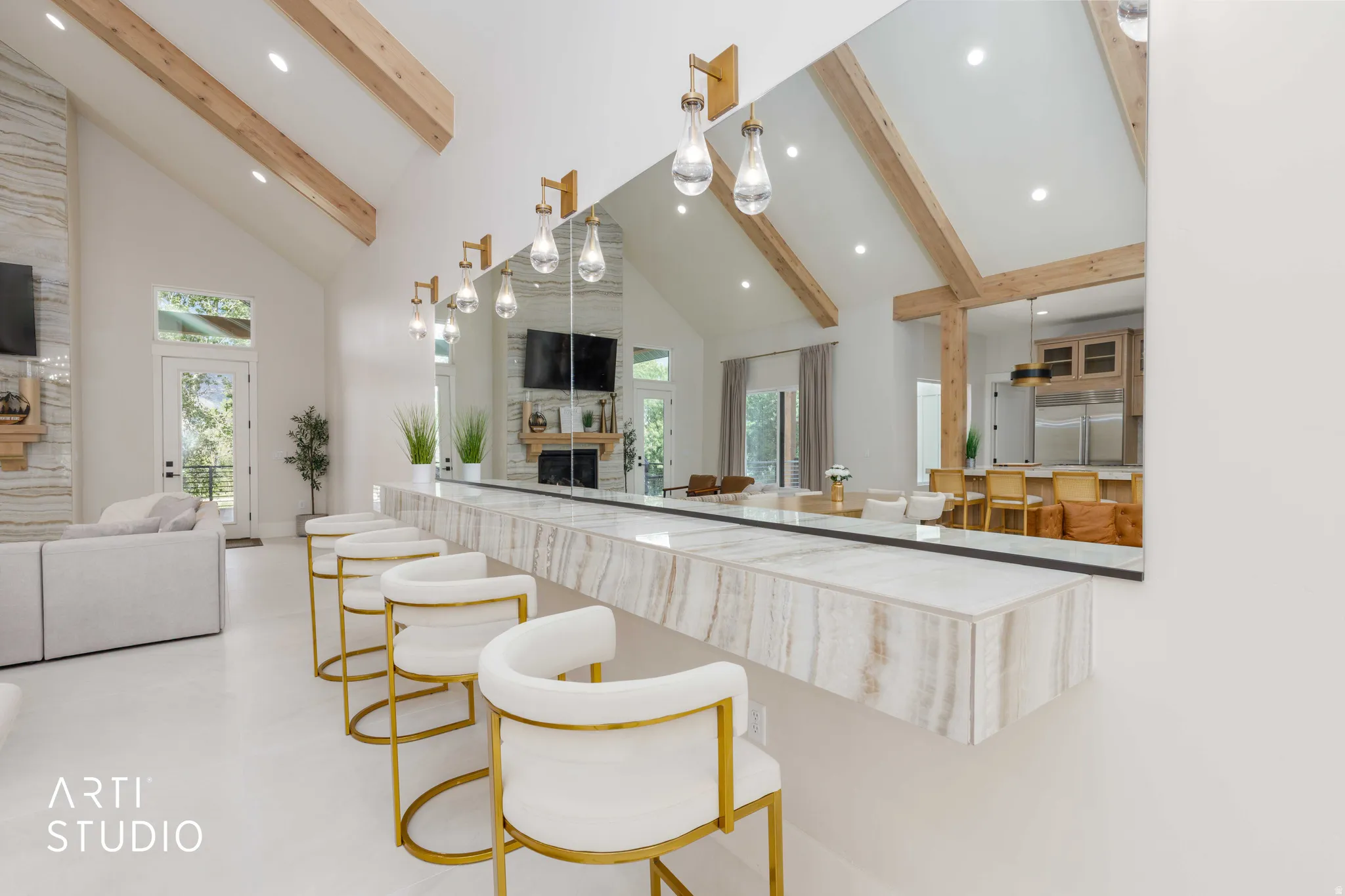 Expansive great room featuring a floating stone bar with pendant lighting, vaulted ceilings with exposed wood beams, a floor-to-ceiling stone fireplace, and light-tone flooring