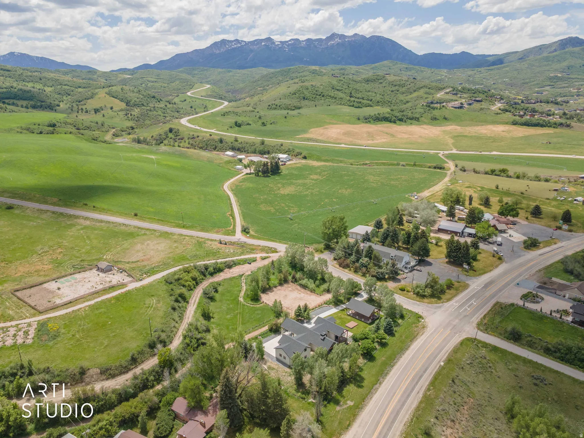 Aerial perspective showcasing expansive green fields, established roads, and distant snow-capped mountains