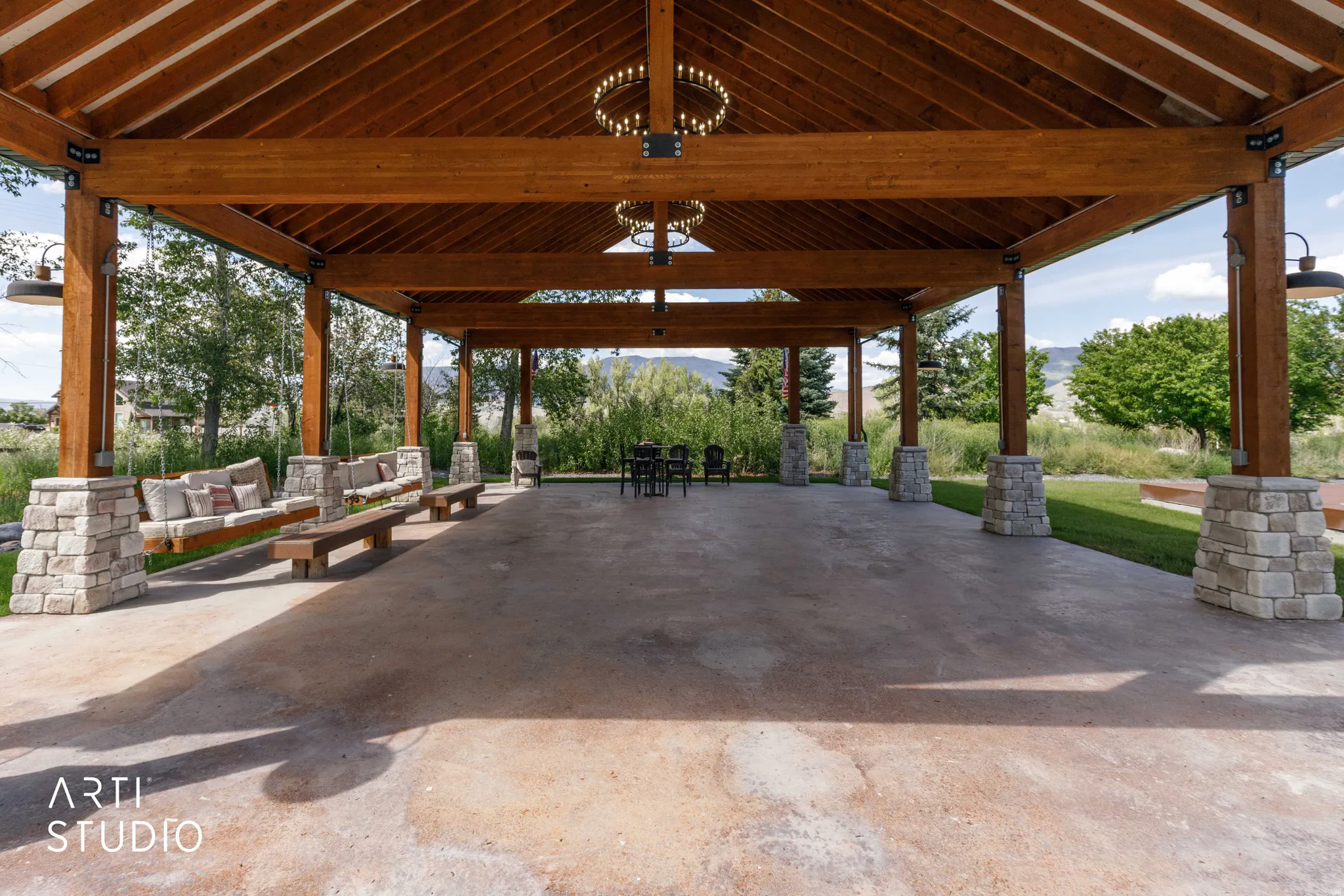 Expansive covered patio featuring a wood-beam ceiling, stone-wrapped columns, concrete flooring, and built-in swing seating