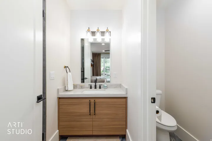 Bathroom featuring a wood-finish vanity with dual doors, a stone countertop, an integrated sink with a matte black faucet, and a rectangular mirror