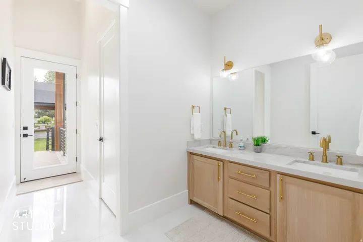 Double vanity with light wood-finish cabinetry, white countertop, and gold-finish fixtures