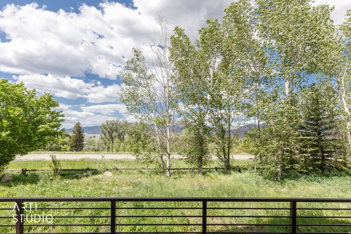 Expansive outdoor scenery featuring mature trees, a grassy field, and distant mountains under a blue sky with white clouds