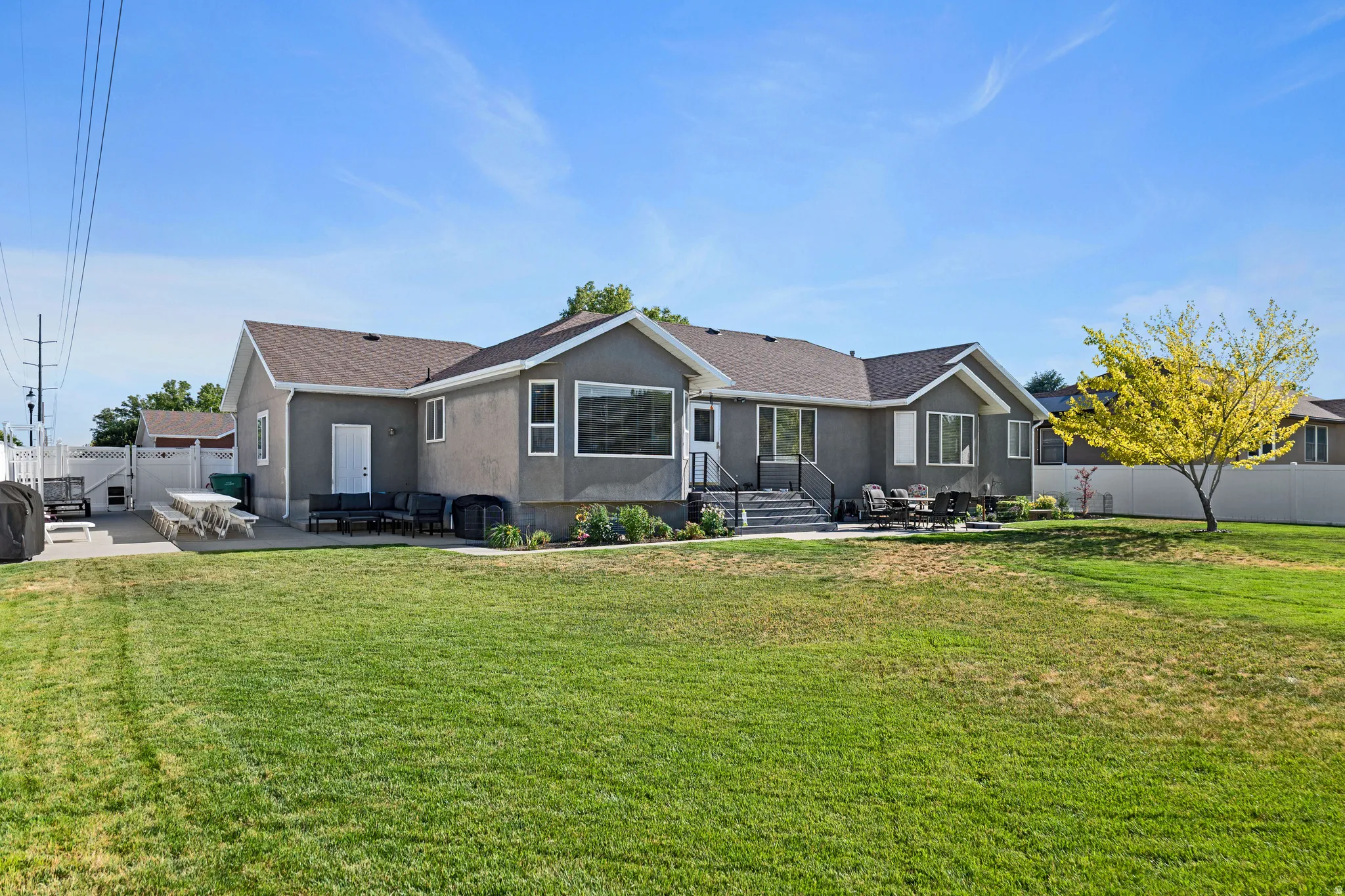 Expansive rear yard featuring a concrete patio, mature tree, and a stucco exterior.