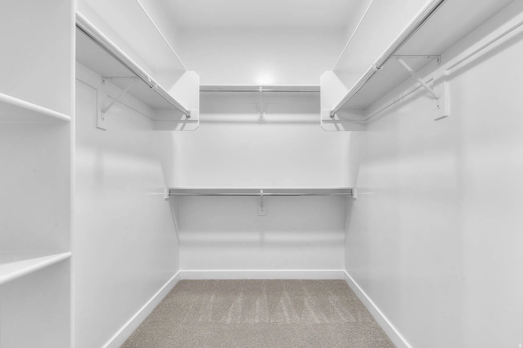 Spacious walk-in closet featuring white built-in shelving, multiple hanging rods, and light gray carpet flooring