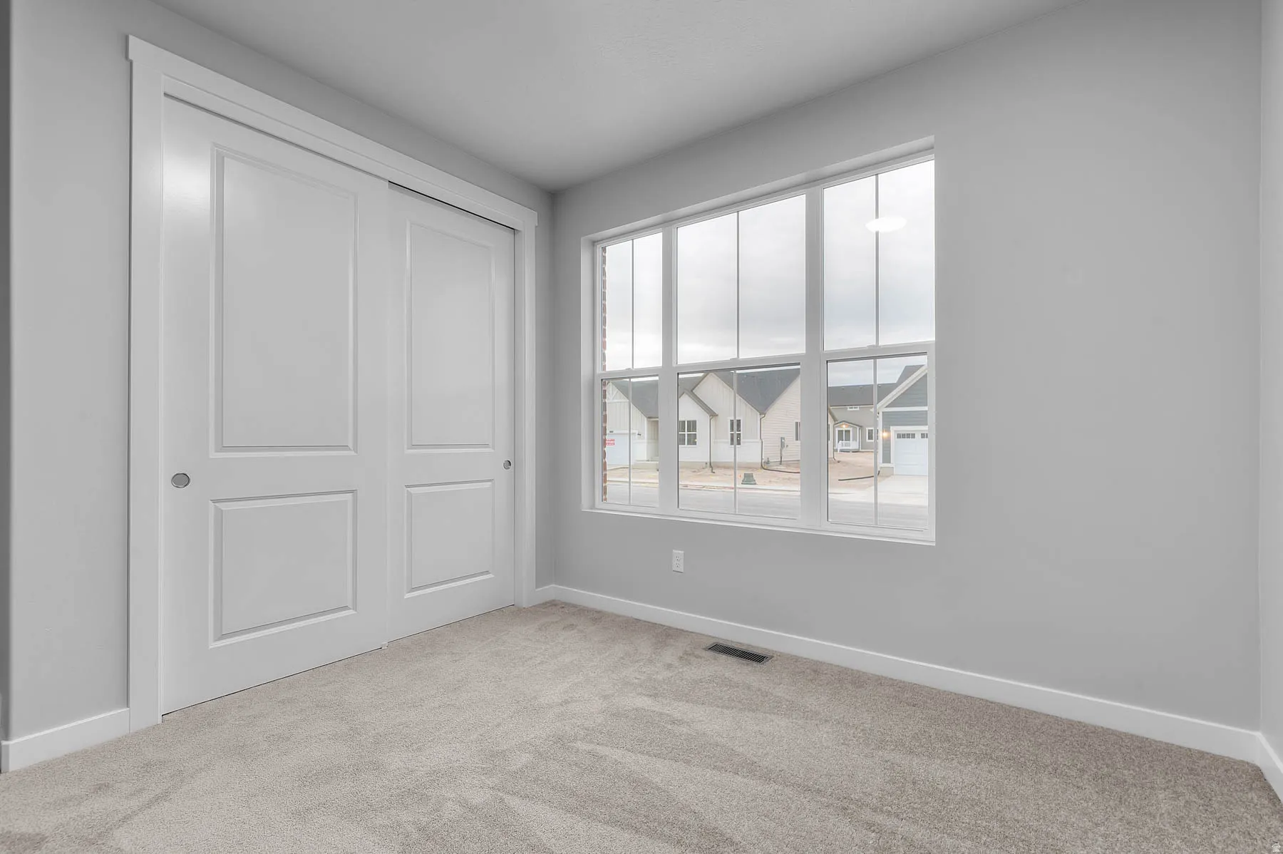 Carpeted room featuring a multi-pane window, white trim, light gray walls, and a two-panel sliding closet door