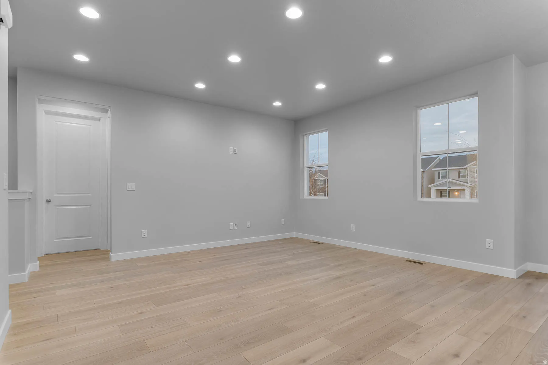 Spacious room featuring light wood-finish flooring, recessed lighting, and multiple windows