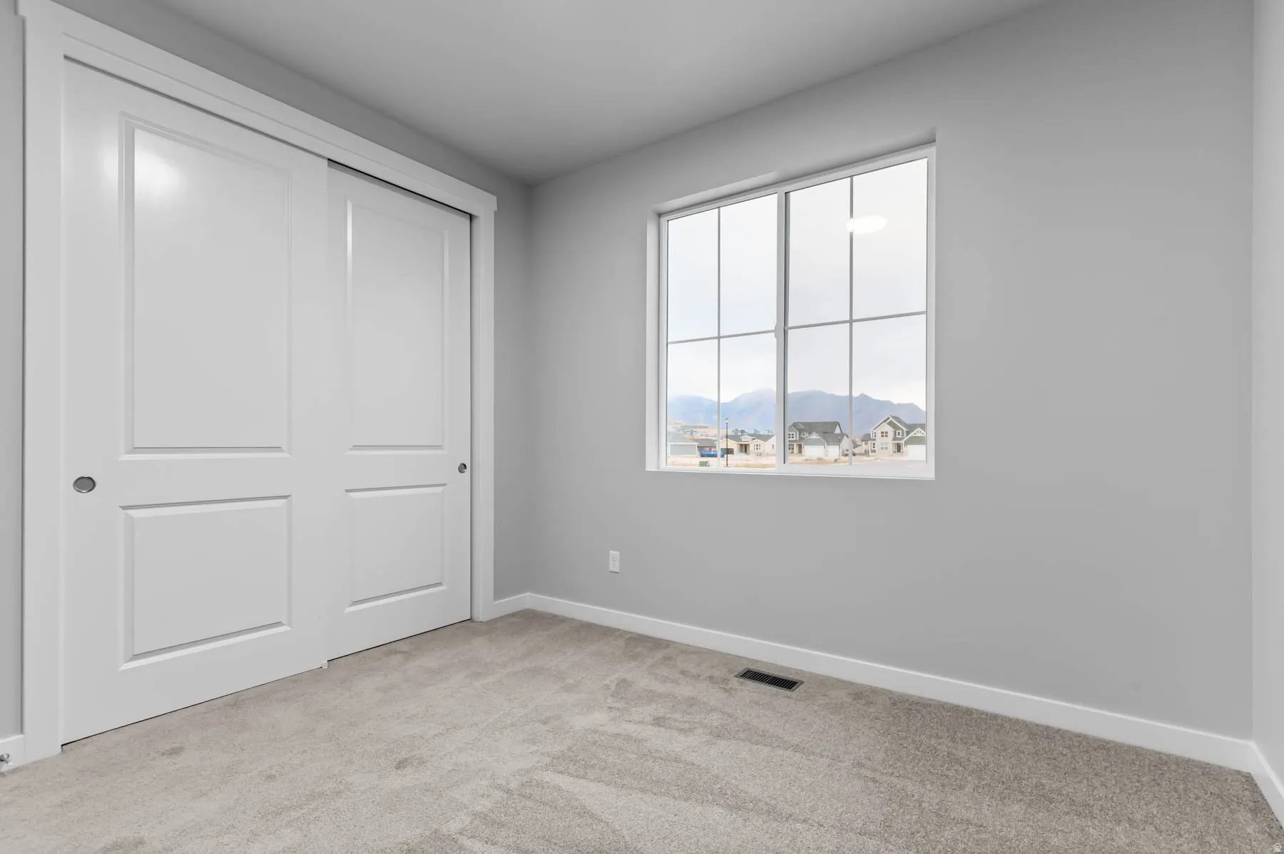 Bedroom featuring light gray walls, plush carpet flooring, a large window with white muntins, and a dual sliding closet with white panel doors