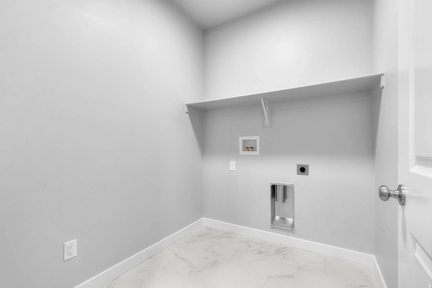 Laundry area featuring a built-in shelf, white baseboards, and light-toned tile flooring
