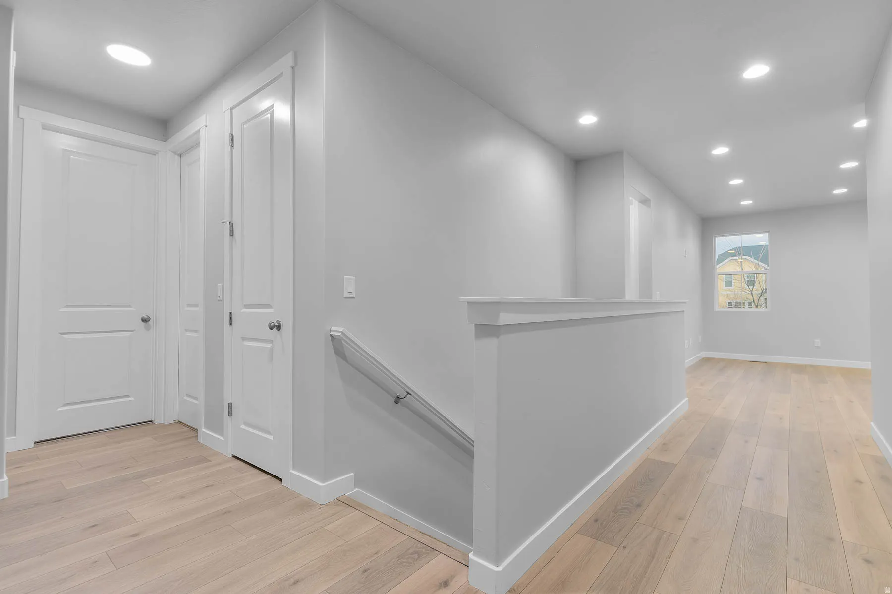 Spacious landing featuring light wood-finish flooring, recessed lighting, white baseboards, and a contemporary staircase railing