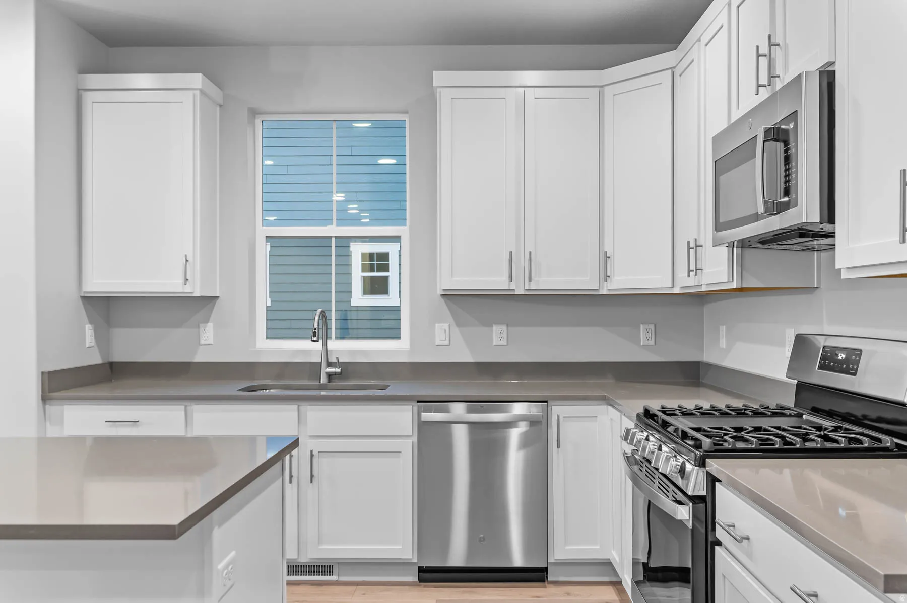 Modern kitchen featuring white shaker cabinetry, stainless steel appliances, light wood-finish flooring, and light gray countertops
