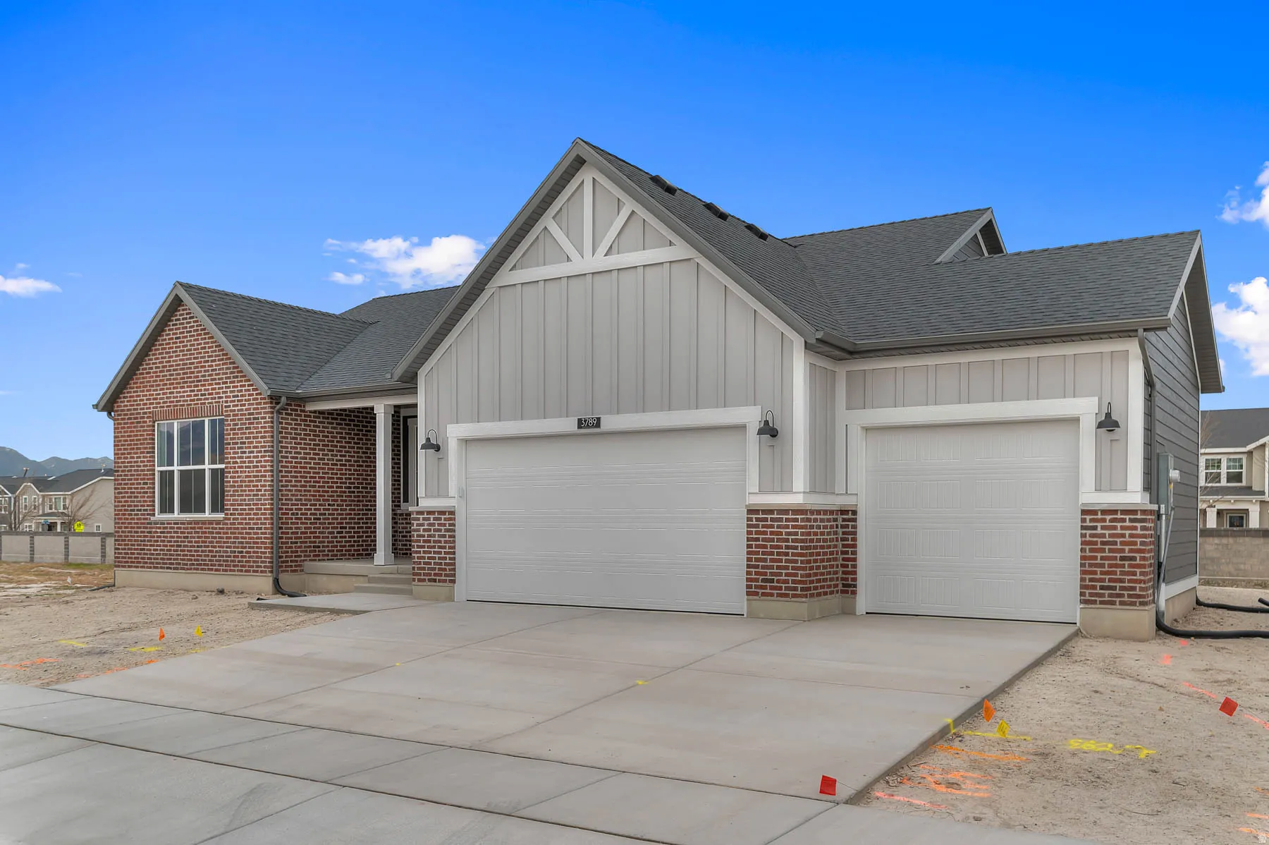 Contemporary architectural exterior featuring a blend of brick and light gray siding, a dark shingle roof, a prominent two-car garage, and a covered entryway