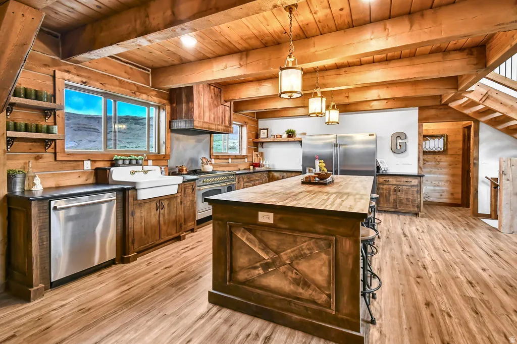 Open-concept kitchen featuring wood-finish flooring, exposed wood beam ceiling, custom wood cabinetry, a central island with bar seating, and stainless steel appliances