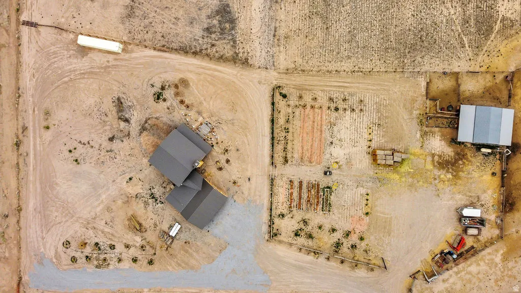 Aerial perspective showcasing a property with a main residence featuring a dark-toned roof, a separate outbuilding with a metal roof, and designated areas for cultivation
