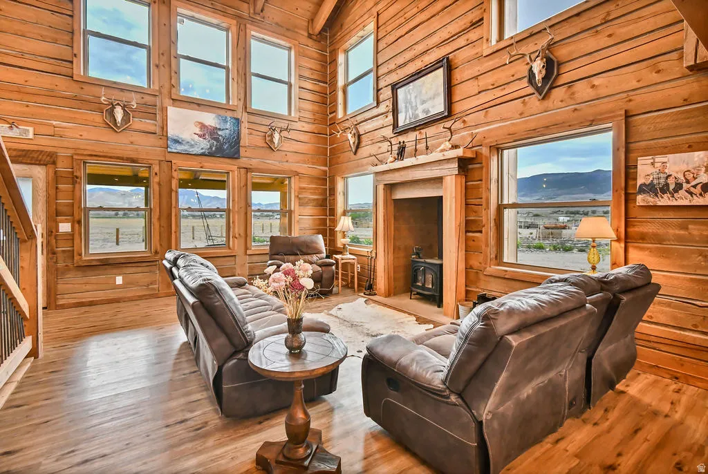 Vaulted living space featuring extensive wood-finish wall paneling, wood-finish flooring, a wood-burning stove, and multiple large windows with mountain scenery